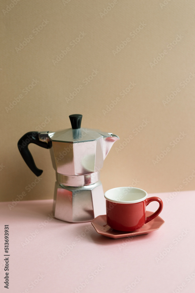 Italian coffee maker mocha coffee pot and cup on pink table. beige wall background