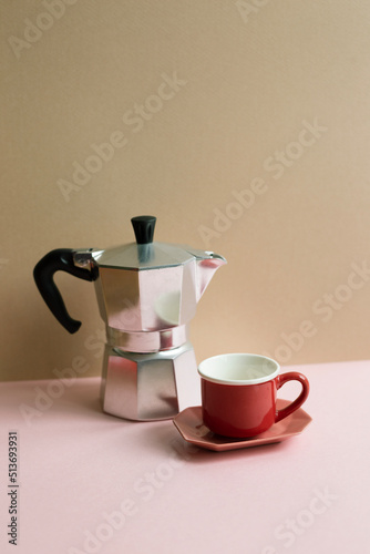 Italian coffee maker mocha coffee pot and cup on pink table. beige wall background