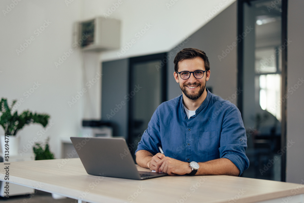 Portrait of a smiling man, posing for the camera while working online. Portrait of a smiling man, posing for the camera while working online.