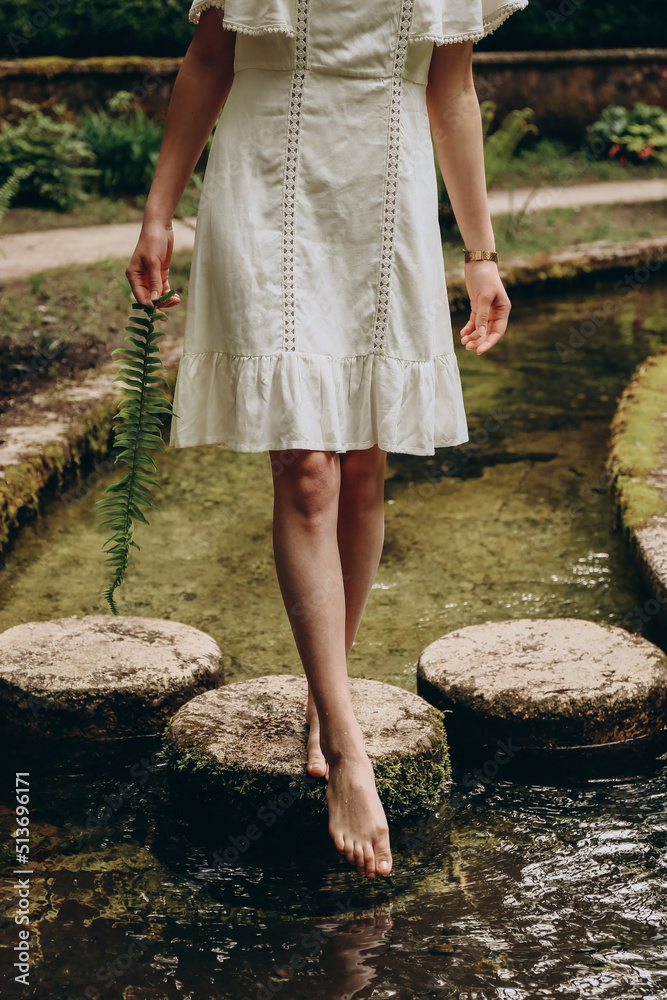 Woman with fern in hands standing on stones and trying water on summer day. Summer nature concept