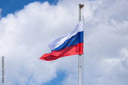 flag of Russia on a flagpole against a blue sky with clouds