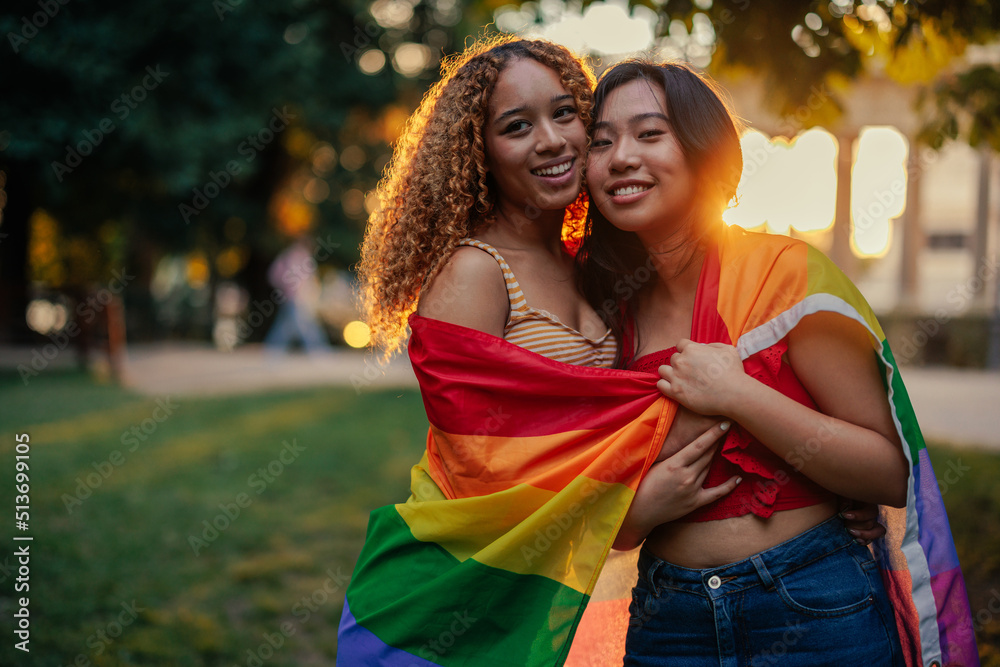 Front view of lesbian couple embracing and holding rainbow flag Front view of lesbian couple embracing and holding rainbow flag