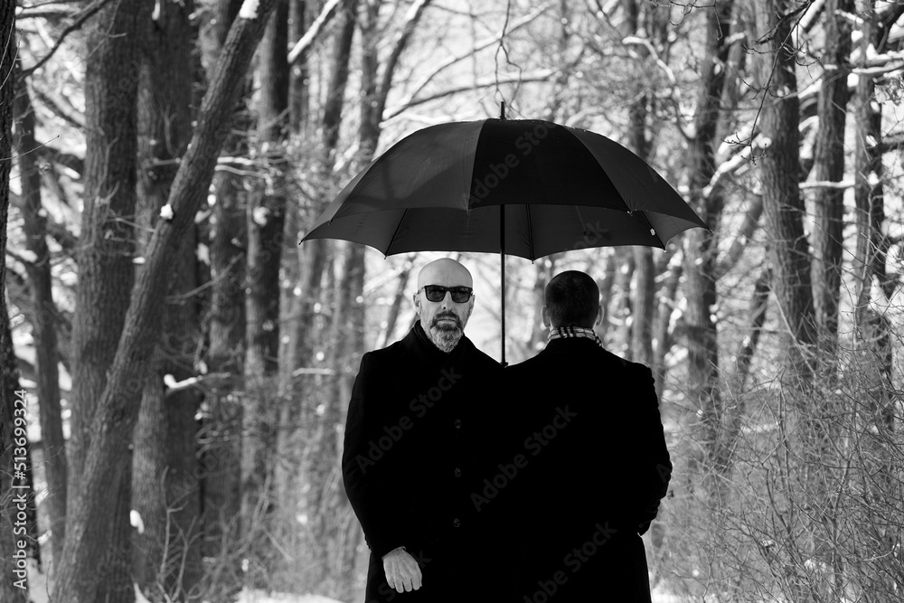 portrait of two men under an umbrella in the park during a snowfall