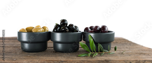 Different varieties of olives on rustic wooden table with olive branch isolated on white background. Horizontal close-up.