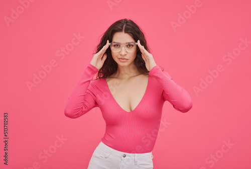 Portrait of cheeky girl in pink in stylish eyeglasses standing against pink background photo