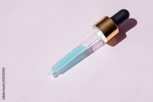 Golden pipette dropper with blue serum made of natural marine collagen on pink background.