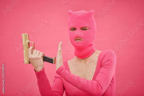 Принти на полотні Portrait of criminal girl in pink balaclava holding gun and looking at camera, s
