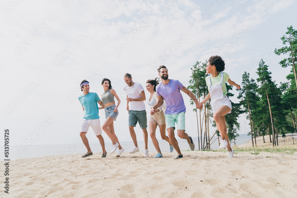 Full body photo of cheery energetic group of best friends running on sandy beach enjoy summer vacation near sea