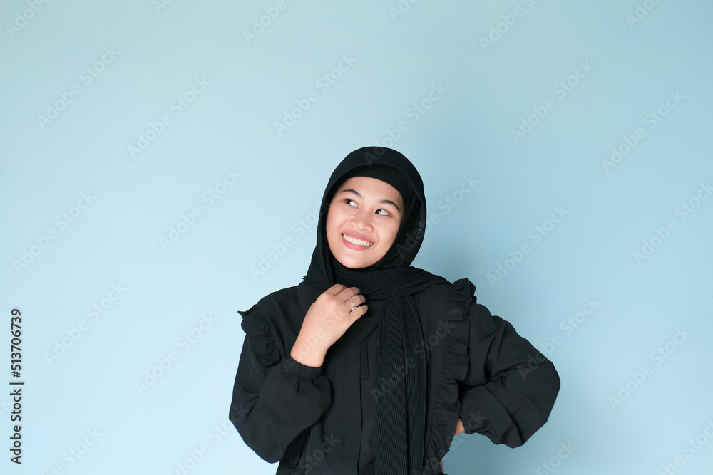 Happy expression of beautiful Asian girl in hijab in black shirt on light blue background Happy expression of beautiful Asian girl in hijab in black shirt on light blue background