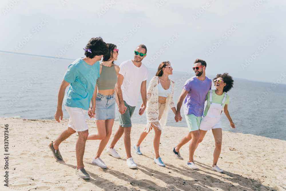 Full length portrait of six carefree peaceful fellows hold hands walking sand beach enjoy weekend outdoors