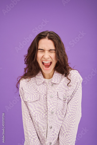 Portrait of young woman expressing her emotion by screaming isolated on purple background