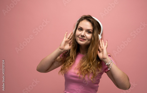 Young woman listening music in headphones with a smile face and stand over pink background. Attractive lady enjoying song copy space. People, music, emotions concept.