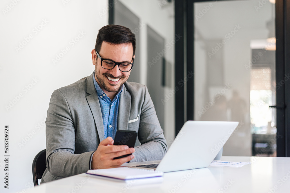 Happy entrepreneur networking on mobile phone while sitting at office desk Happy entrepreneur networking on mobile phone while sitting at office desk