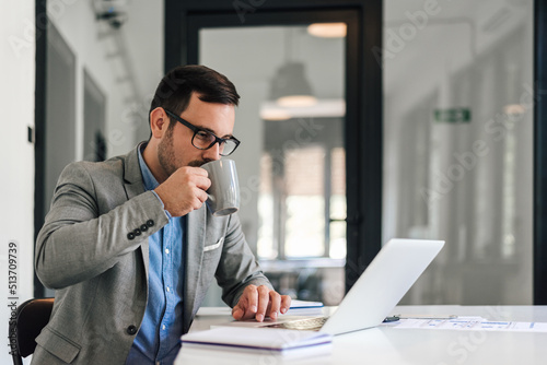 Male manager drinking coffee while working on laptop at desk in office