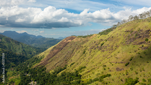 Mountain slopes with tropical forest and tea plantations under blue sky and clouds. Sri Lanka.