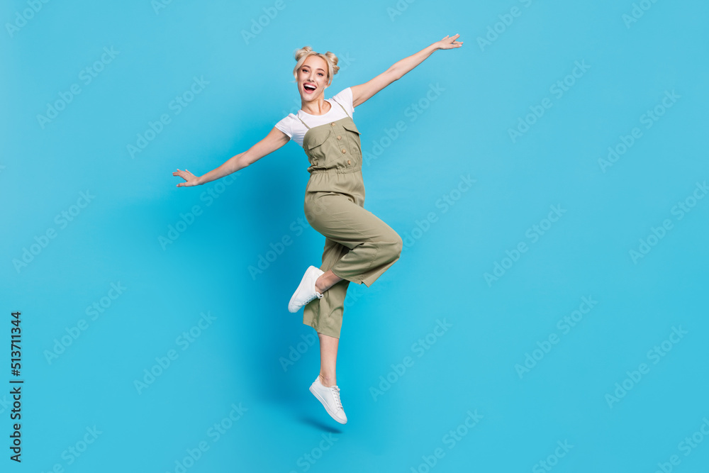 Full size photo of funky young lady jump wear t-shirt grey overall shoes isolated on blue background