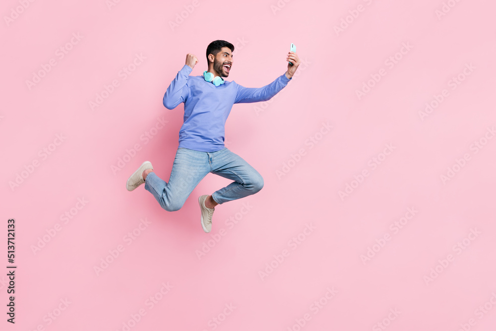 Full length photo of funny lucky arabian man wear long sleeve shirt blogging gadget jumping running isolated pink color background