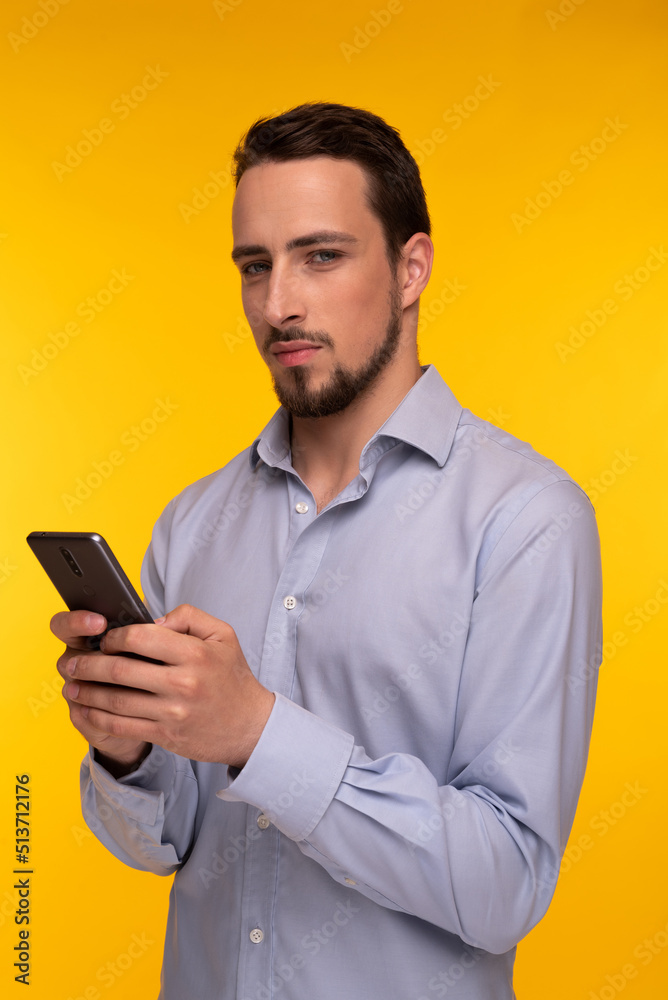 A guy in a blue shirt holds a mobile phone in his hands and looks with a smirk A guy in a blue shirt holds a mobile phone in his hands and looks with a smirk