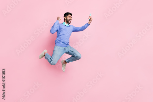 Full length photo of funny lucky arabian man wear long sleeve shirt blogging gadget jumping running isolated pink color background