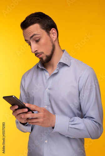 A guy in a blue shirt holds a mobile phone in his hands and looks into it