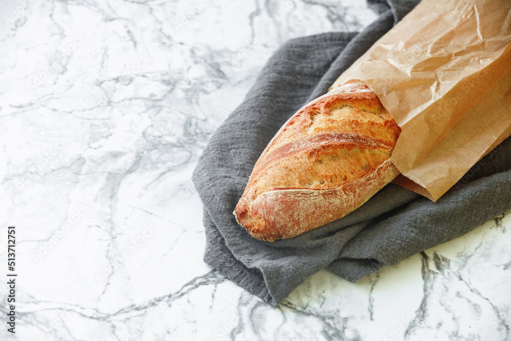 Rustic sourdough baguette on kitchen towel on marble table. Free space for text Rustic sourdough baguette on kitchen towel on marble table. Free space for text