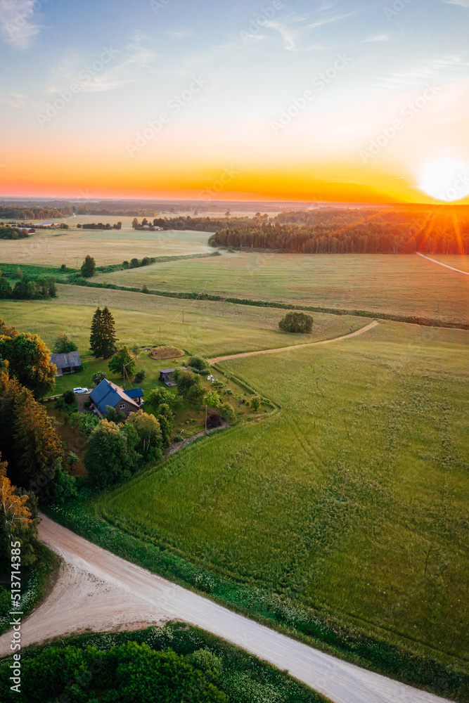 Aerial view over countryside at warm sunrise tones. Agriculture land mixing with forest and meadows.