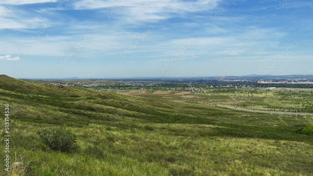 View of the city of Ust-Kamenogorsk (kazakhstan). Summer steppe. Green grass and blue sky. Hills. Cityscape