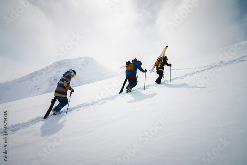 Fotografia Three friends snowboarders skiers go uphill with a snowboard and skis in their h