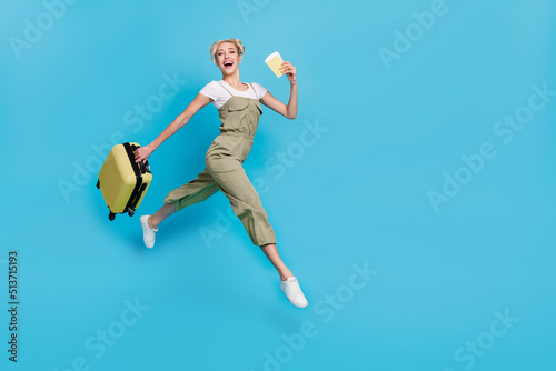 Full length photo of impressed young blond lady run with bag passport wear t-shirt overall sneakers isolated on blue background © deagreez