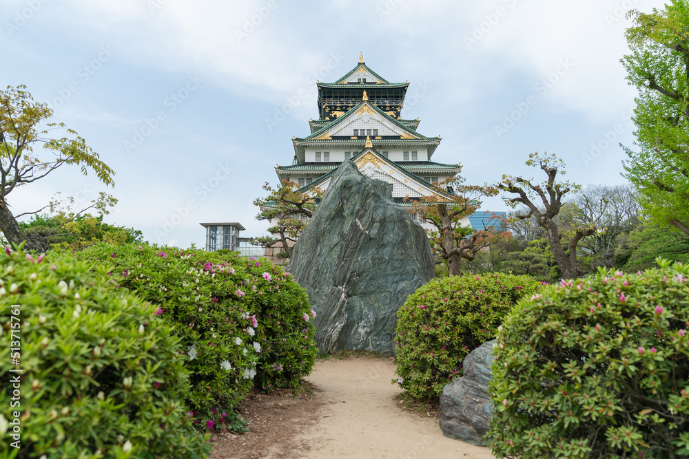 beautiful Osaka castle at distance against sunny blue sky and blocked by a rock at the end of bush garden path in japan