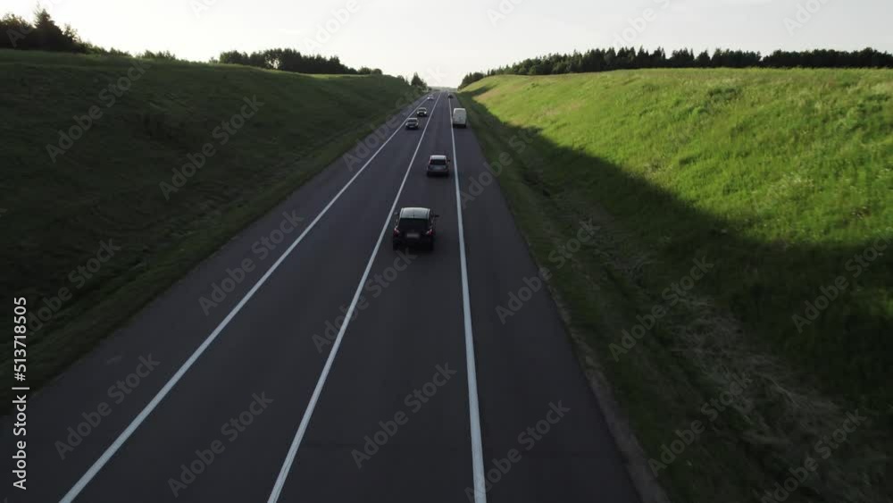 Aerial shot, the drone follows cars that move along the asphalt highway running across rural at sunset in summer. Concept of traveling by car, camping, long trips to new places. Aerial shot, the drone follows cars that move along the asphalt highway running across rural at sunset in summer. Concept of traveling by car, camping, long trips to new places.