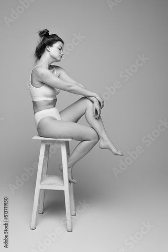 Studio portrait of young beautiful woman with slim body sitting on chair, posing in underwear. Black and white photography