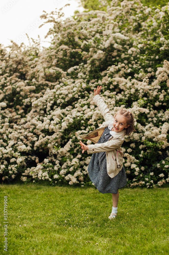 cute little girl is making funny pose in front of the huge bush with little white flowers