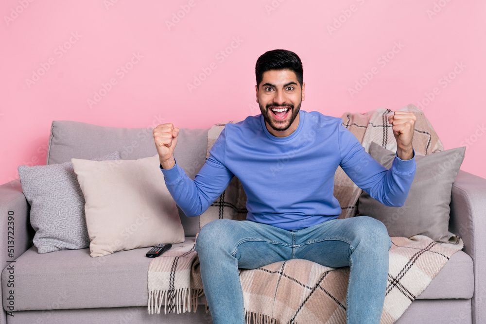 Photo of funny delighted handsome guy sit couch raise fists celebrate success triumph isolated on pink color background