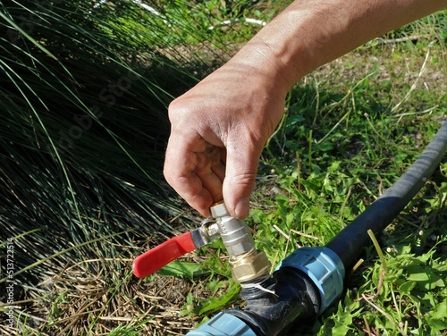 male hand fixing water faucet on garden plastic pipe connection for watering on green sunny lawn close-up, valve installation in garden watering system