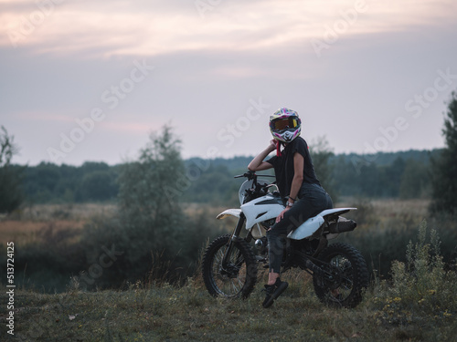 A young slender woman in a helmet on a cross - country motorcycle or pit bike . Moto woman