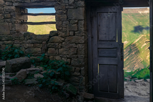 Bild auf Leinwand wooden door in the ruins of an abandoned house through which mountains are visib