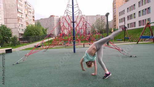 A teenager child makes an acrobatic wheel on a playground for games. The relief muscles of the press are clearly visible