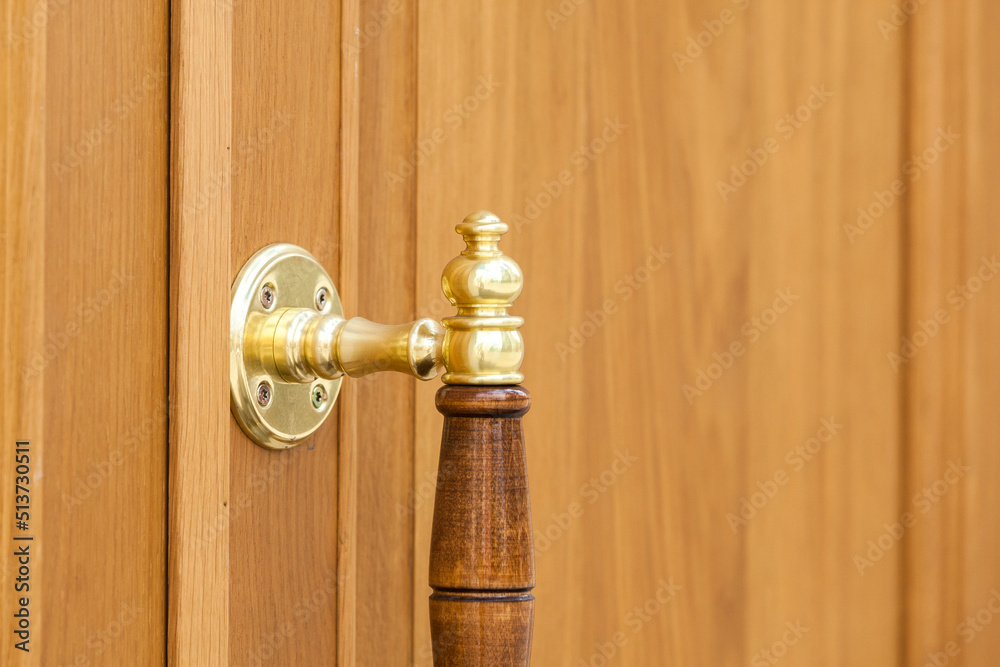 Fragment of a yellow metal gilded door handle against a yellow wooden door Fragment of a yellow metal gilded door handle against a yellow wooden door