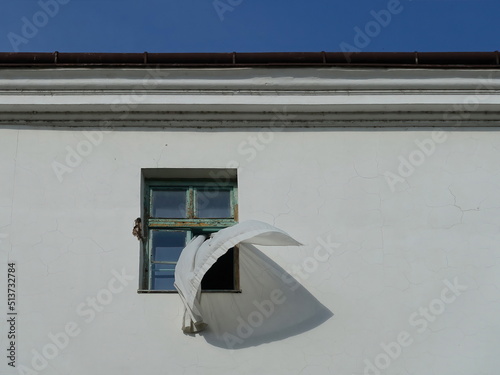 A loose curtain blows out of the window