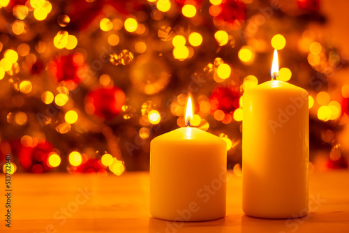 Two burning candles on wooden table on background of decorated christmas tree bright in lights. Christmas celebration  festive atmosphere