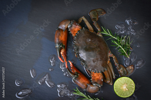 raw crab on black background , fresh mud crab with ice and with herbs and spices rosemary lemon lime for cooking food in the seafood restaurant