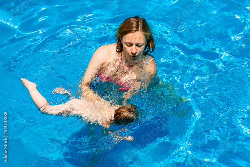 Happy child is having fun. Family happiness. Summer outdoor fun in the pool in the villa. Mom and daughter in the pool. A woman teaches a baby to float on the water and swim
