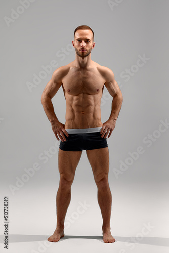 Young male athlete posing. Handsome athletic male power guy. Fitness muscular person. Young athlete showing muscles in the studio, posing shirtless on gray background.