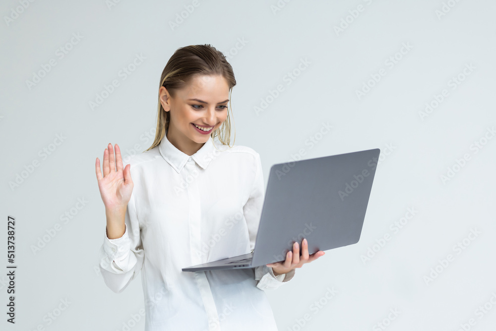 Hi. Beautiful woman waving hand, gesturing hello to laptop screen, video call with friend, communicating online isolated on gray background. Hi. Beautiful woman waving hand, gesturing hello to laptop screen, video call with friend, communicating online isolated on gray background.