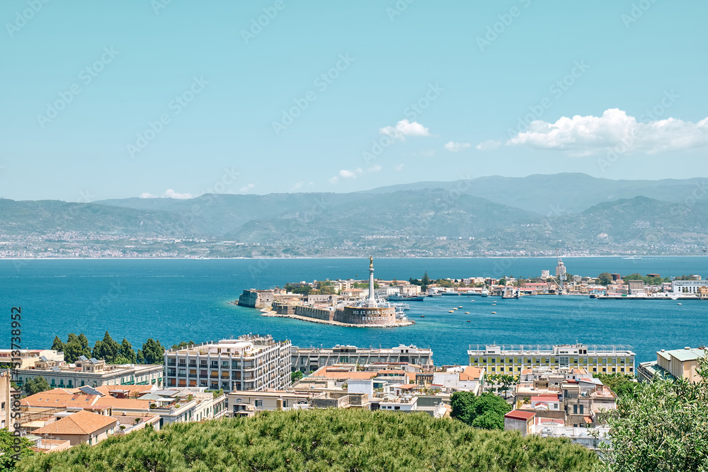 Messina, Sicily, Italy - May 31, 2022:Panoramic view of port of Messina with moored boats, gold Madonna della Lettera statue and calabria coastline in background.