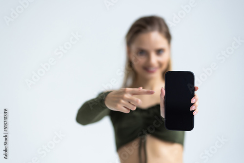 Portrait of a joyful woman pointing finger at blank screen mobile phone and looking at camera isolated over white background