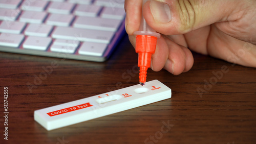 A man performs an at-home COVID-19 test at his desk with a rapid test kit.  	