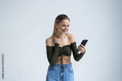 Portrait of a happy joyful woman holding mobile phone and celebrating a win isolated over white background