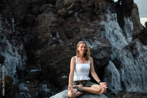 beautiful woman sitting in meditation against dark rocks